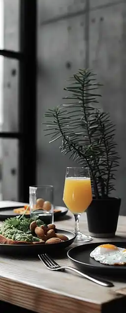 A gourmet breakfast spread on a rustic wooden table: avocado toast, poached eggs, fresh orange juice in glass, soft morning sunlight from the left, depth of field highlighting crispy textures