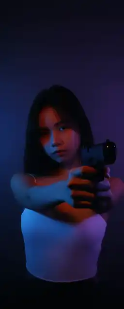 asian girl with prominently feminine body shape holding a gun towards the camera