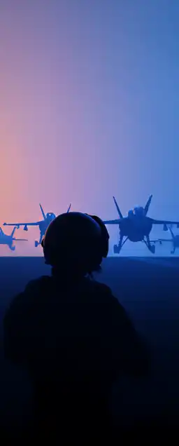a fighter jet pilot with his helmet standing on an aircraft carrier with fighter jets launching in the background