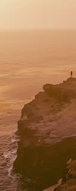 person standing on an edge of a cliff on the ocean