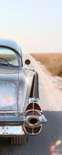 Desert road at golden hour, a single vintage car parked on the side, heat haze warping the horizon, lens flare across the hood, dreamlike soft focus on the distance